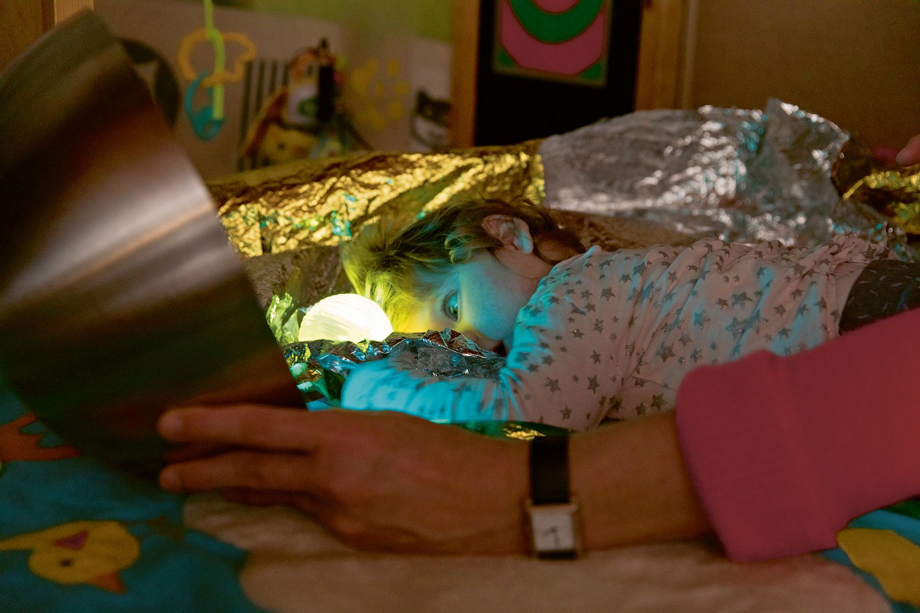 Ismini liegt im Schlafanzug mit einer Leuchtkugel unter einer Rettungsdecke.