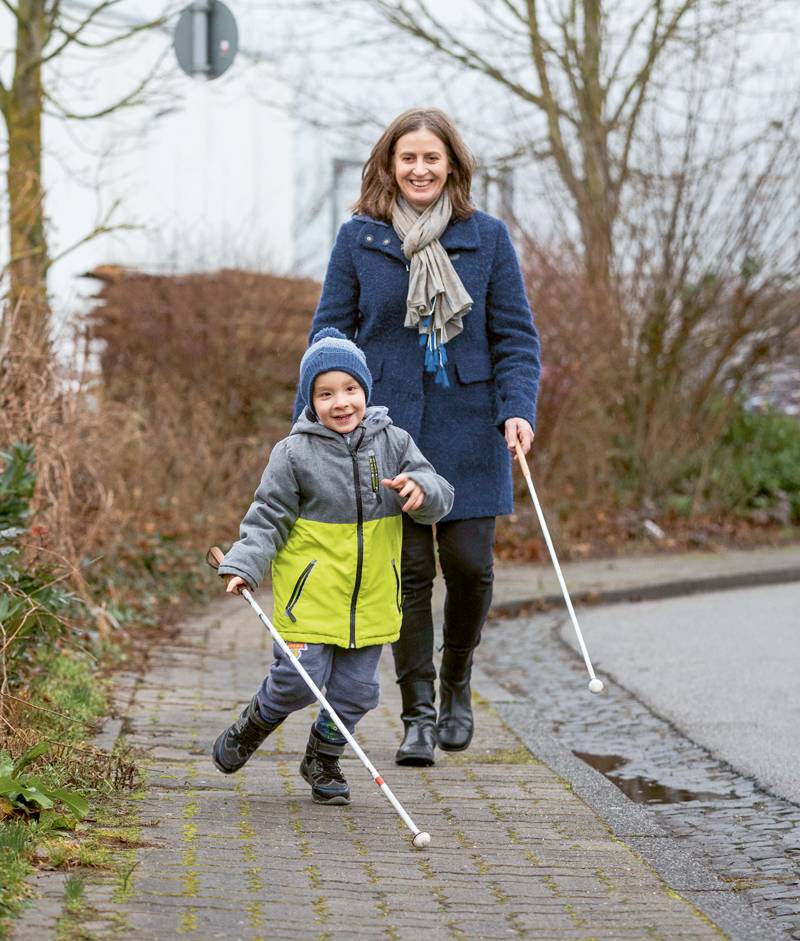 Marie Wiesner übt mit einem kleinen Jungen in grau-gelber Jacke den Umgang mit dem Langstock.