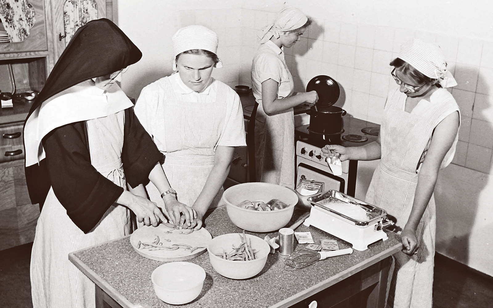 Historisches Schwarz-Weis-Foto. Ordensschwestern mit Schülerinnen der damaligen Blindenschule beim Hauswirtschaftsunterricht