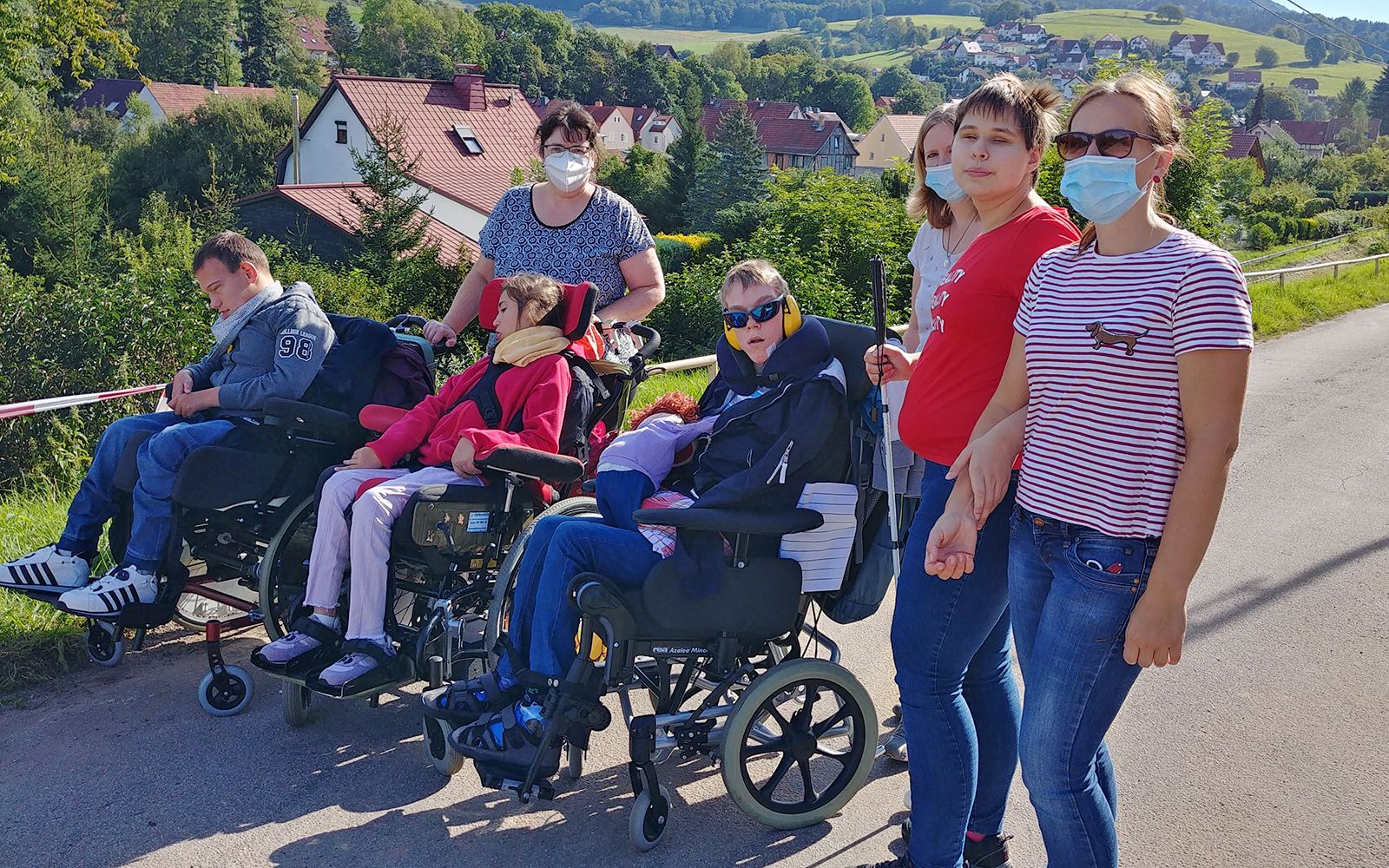 Drei Personen in Rollstühlen, welche von Betreuerinnen begleitet werden.