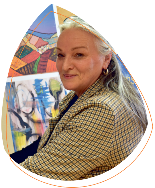 Barbara Knötgen, die ihre Hände auf einem Gemälde hat, das die Kreativgruppe erstellt hat. Es enthält Erhebungen, die haptisch wahrgenommen werden können. Im Hintergrund sind weitere Gemälde ausgestellt.