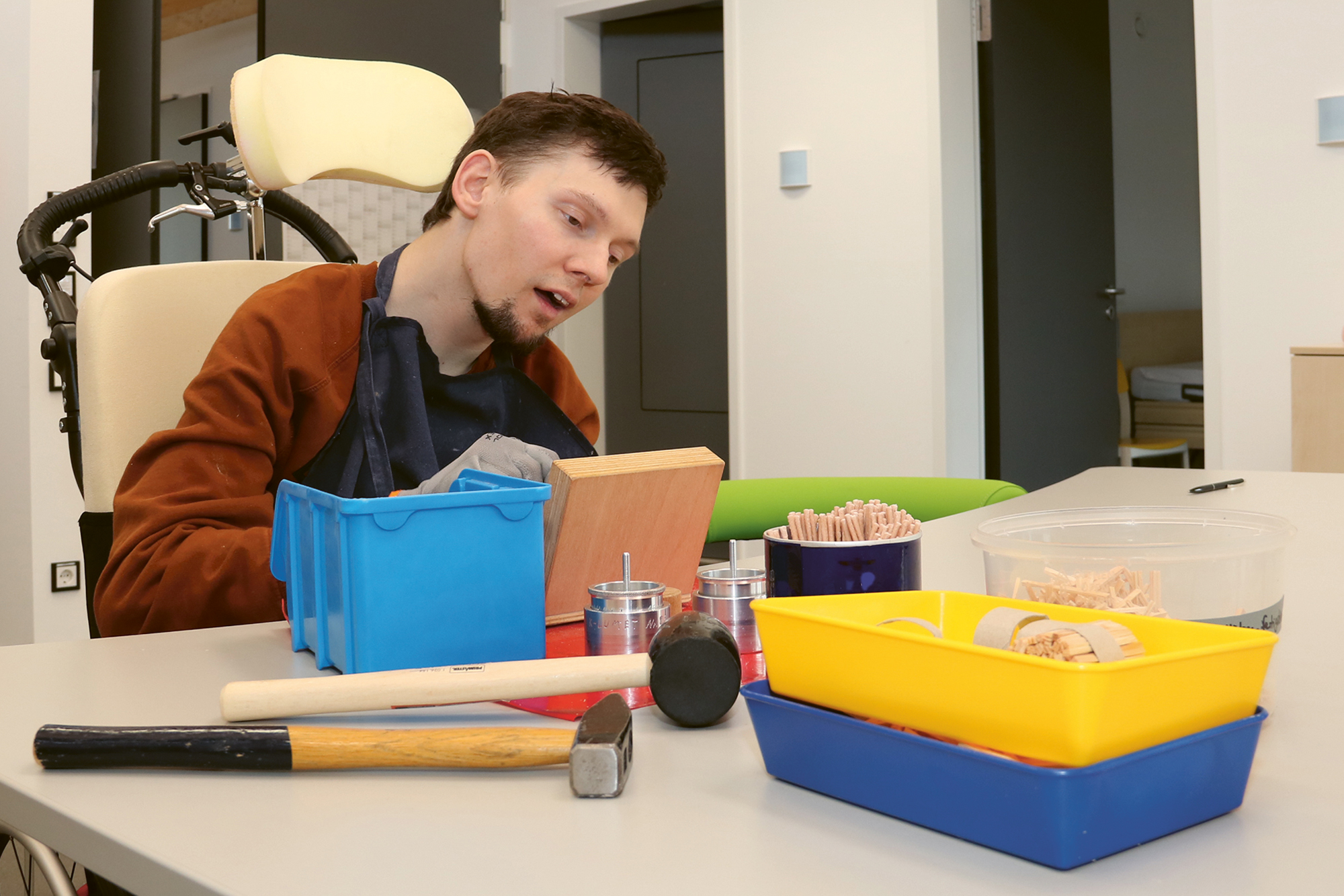 Ein Klient, der Ofenanzünder herstellt. Vor ihm liegen zwei Hammer und mehrere Schachteln. In einigen sind fertig zusammengebaute Ofenanzünder zu sehen.