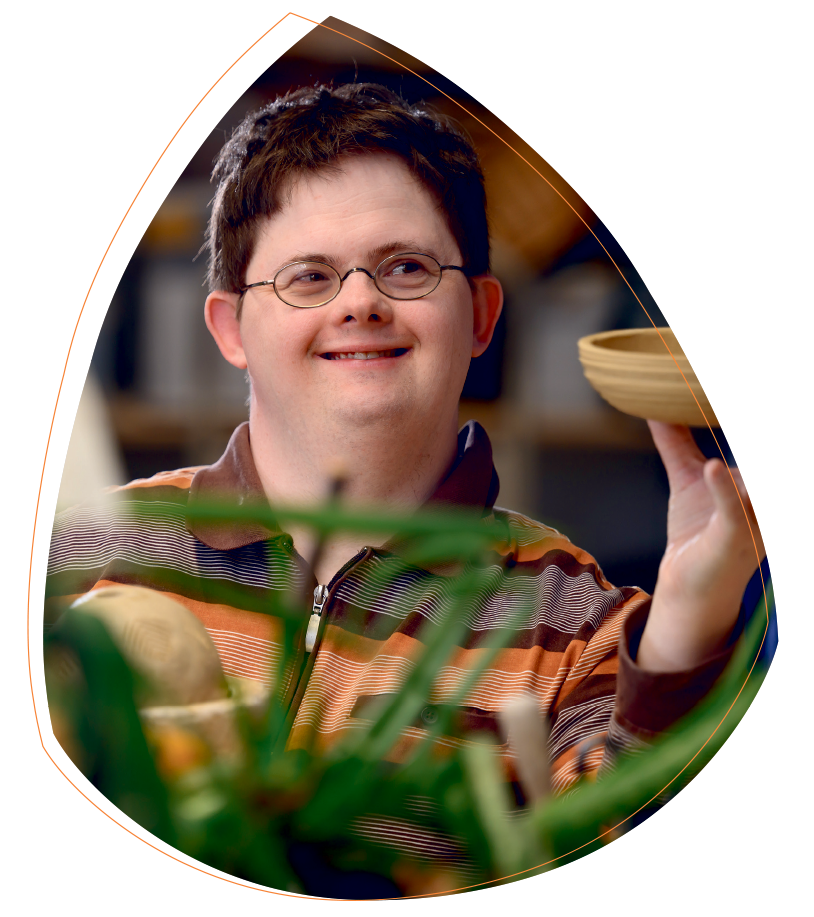 Tobias Teschner arbeitet in der Keramikwerkstatt. Er hält stolz eine getöpferte Schale in der Hand und schaut diese an. Er lächelt.