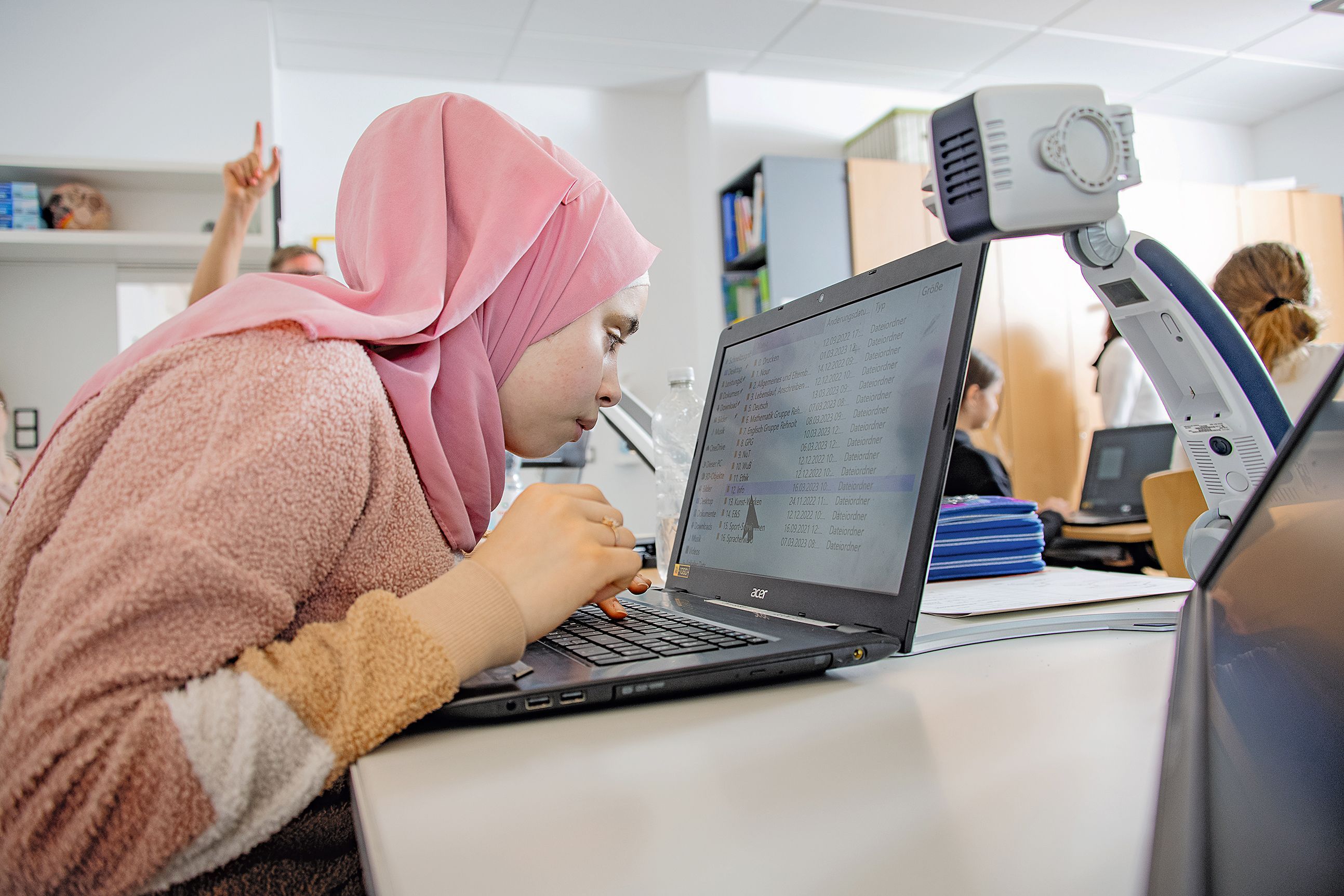 Afan, die über einen Laptop gebeugt ist. Auf dem Bildschirm sind die Inhalte stark vergrößert. Sie trägt ein rosa Kopftuch. 