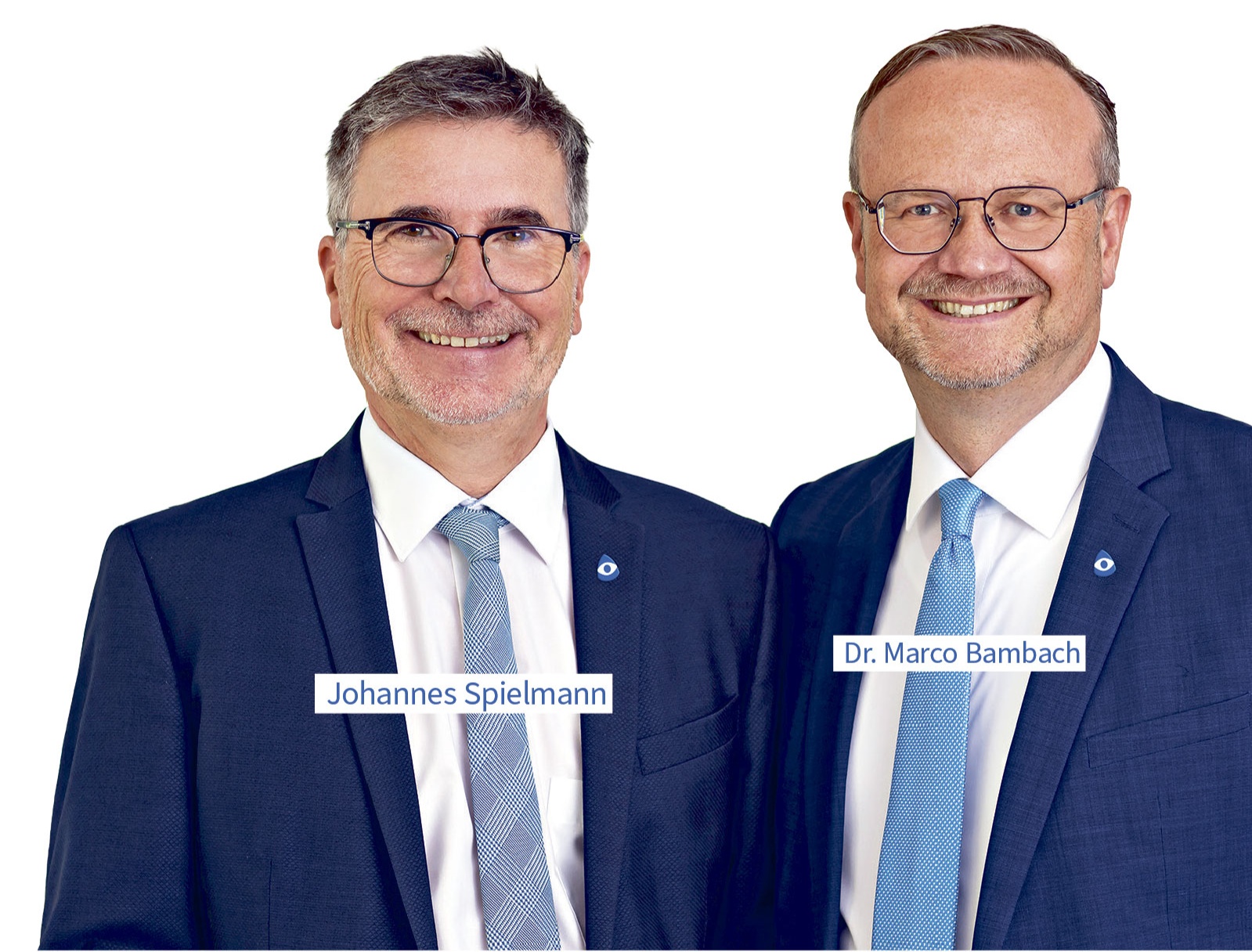 Zwei lächelnde Männer im Anzug stehen nebeneinander vor weißem Hintergrund. Links: Johannes Spielmann. Rechts: Dr. Marco Bambach