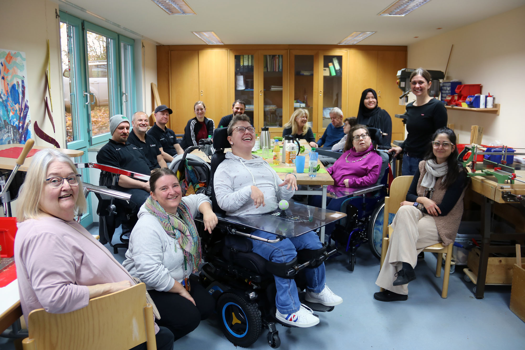 Vierzehn Menschen mit und ohne Behinderung sitzen um einen großen Arbeitstisch und trinken Kaffee.