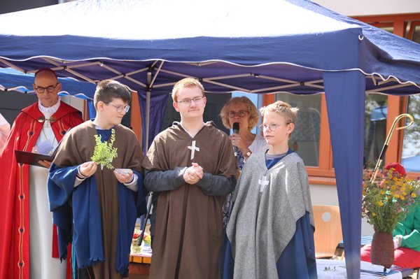 Eine Gruppe von fünf Menschen steht unter einem Pavillon. Links steht der Würzburger Bischof, daneben drei Jungen als Missionare verkleidet und dahinter eine Frau mit Mikrofon.