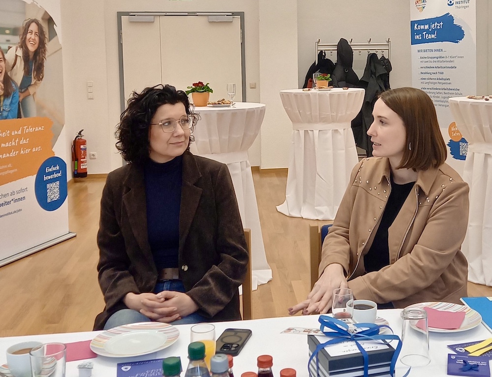 Zwei Frauen sitzen an einem Tisch und unterhalten sich.