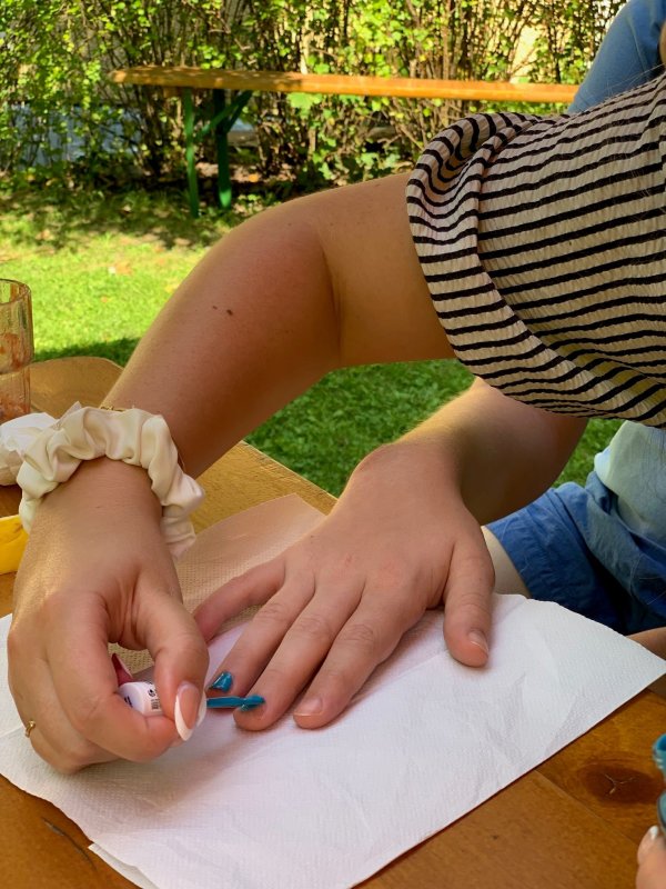 auf dem Bild sieht man, wie eine Hand bei einer anderen Hand die Fingernägel blau lackiert