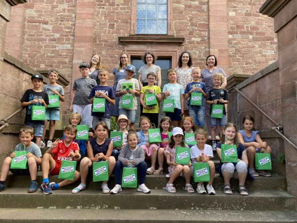 Eine Gruppen von Kommunionkindern sitzt auf Treppenstufen vor einer Kirche.