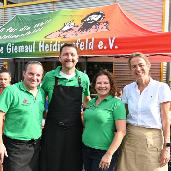 Eine Gruppe von vier Personen steht vor einem Gebäude mit Grillstation.