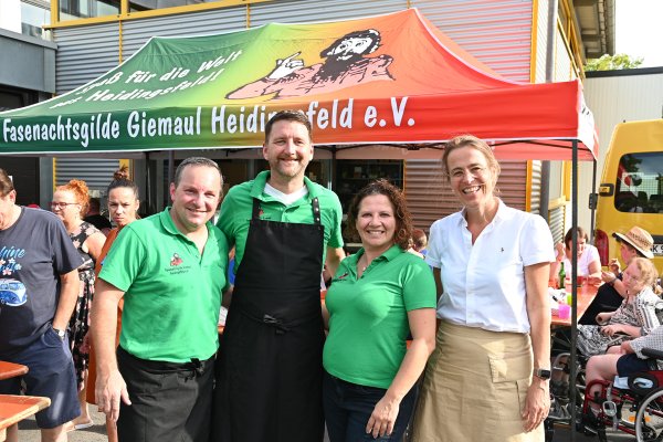 Gruppenbild, das vier Personen vor einem Gebäude mit einem Grillstand zeigt.