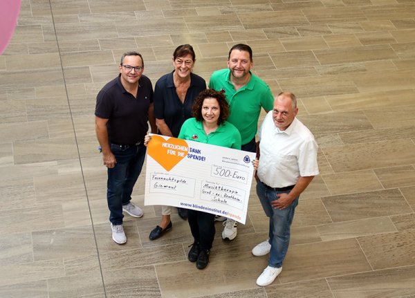 Eiine Gruppe von fünf Menschen hält einen sehr großen Spendenscheck in den Händen.