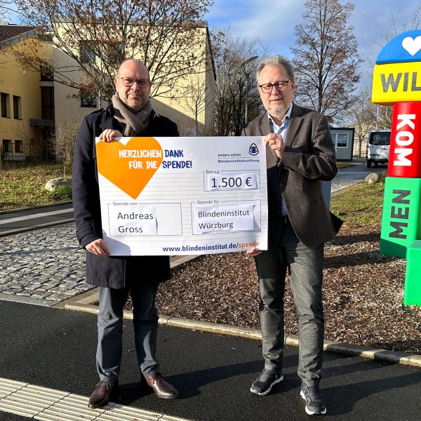 Zwei Männer halten einen riesigen Spendenscheck. Darauf steht, dass Andreas Gross 1.500 Euro für das Blindeninstitut Würzburg spendet.