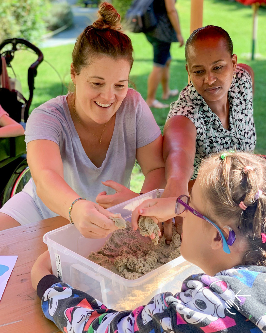 Das Bild zwei Frauen und ein Mädchen, die in einer Schüssel Sand fühlen.