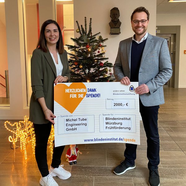 Links im Bild steht eine Frau, rechts im Bild steht ein Mann, dazwischen ist ein Spendenscheck, den beide halten.