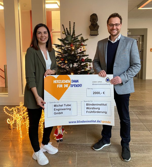 Links im Bild steht eine Frau, rechts im Bild steht ein Mann, dazwischen ist ein Spendenscheck, den beide halten.