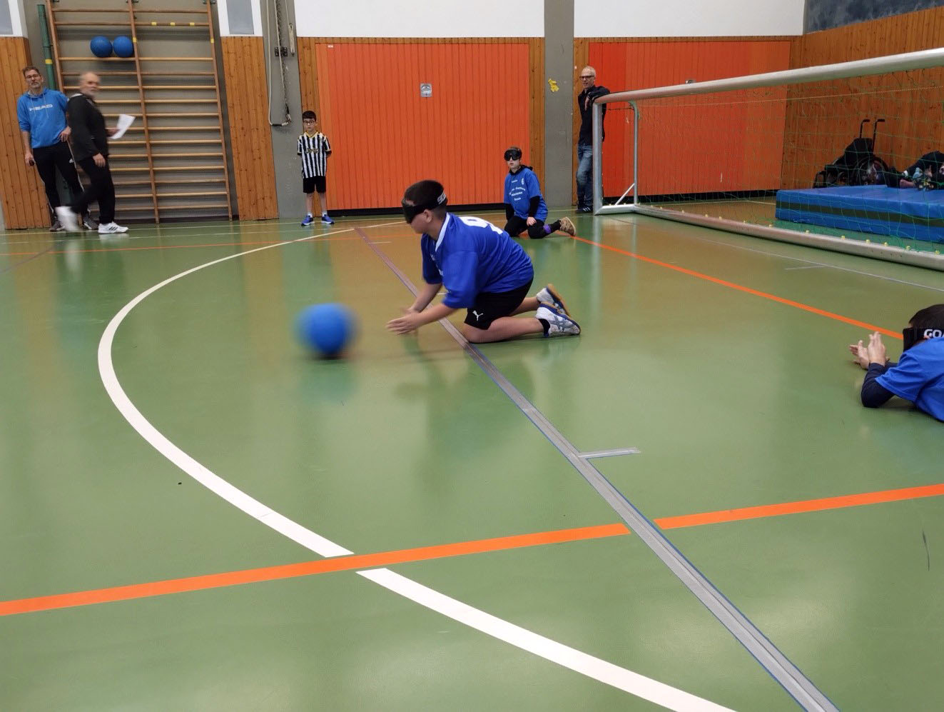 Ein Junge kniet vor einem Goalballtor in einer Sporthalle.