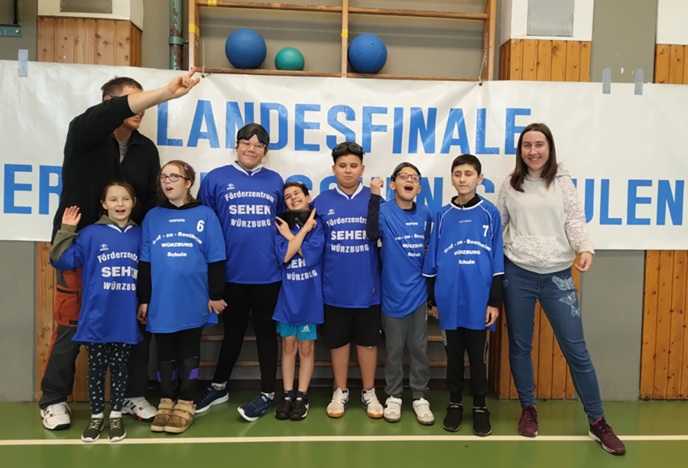 Sieben Grundschüler stehen mit ihren zwei Lehrkräften in einer Sporthalle  im Halbkreis und freuen sich.