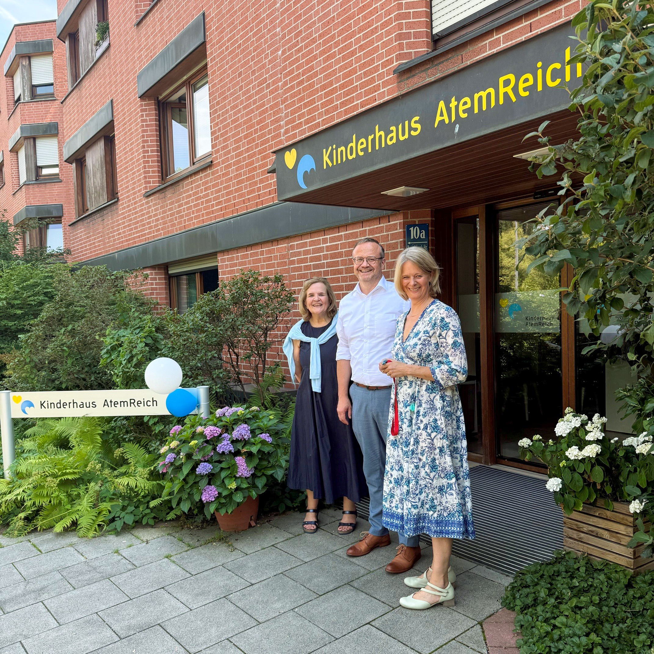 Drei Menschen stehen vor dem Kinderhaus AtemReich. Das Foto wurde seitlich aufgenommen und zeigt von links nach rechts: Felicitas Hanne, Marco Bambach, Barbara Weltin