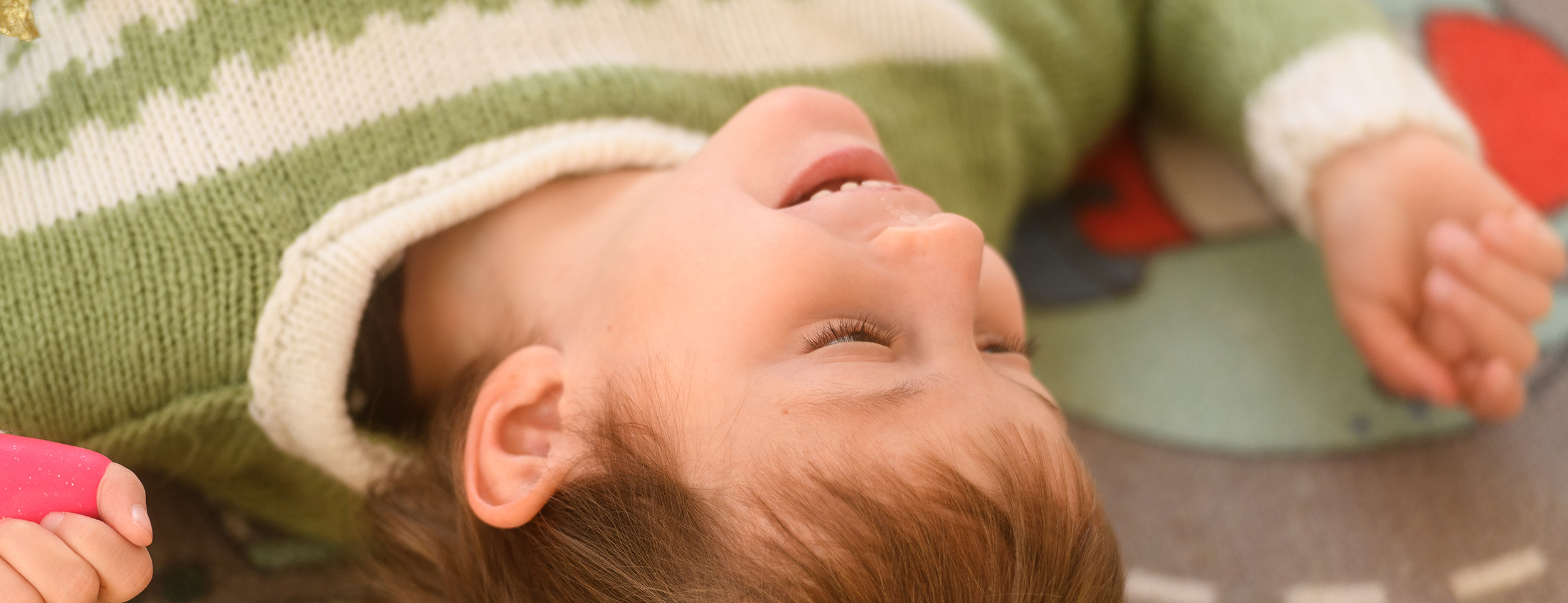 Ein Kind liegt auf einem Spielteppich und lächelt. 