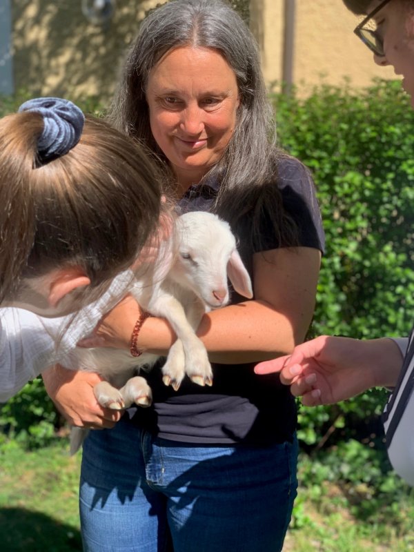 Auf dem Bild sieht man eine Frau mit einem Lämmchen im Arm.