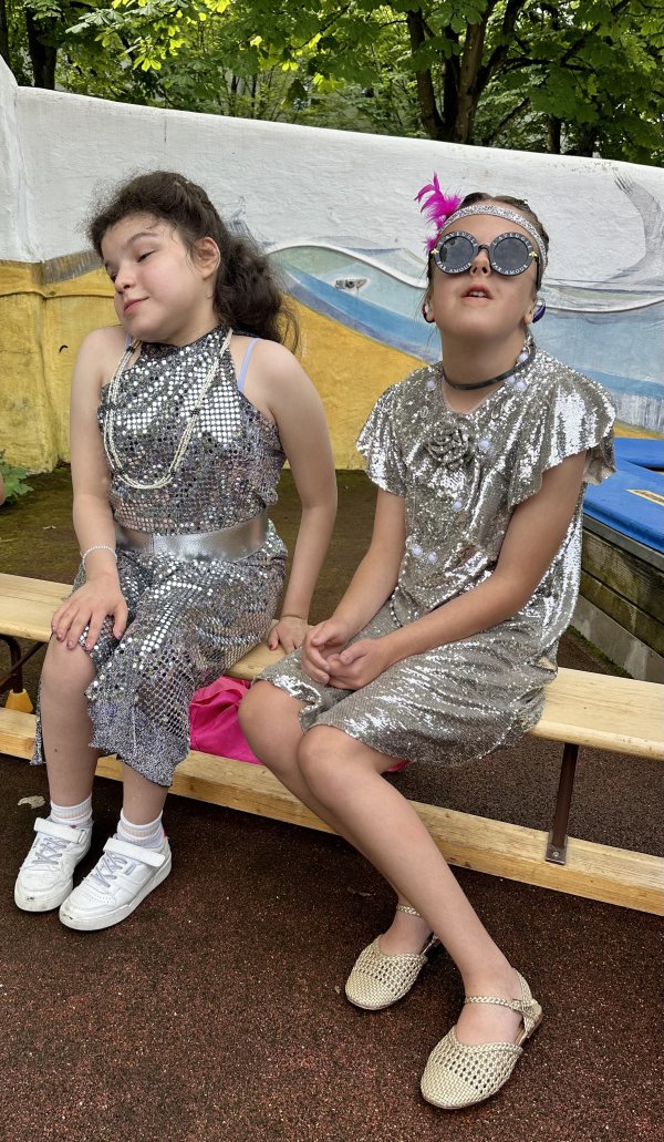 Das Bild zeigt zwei Mädchen mit silber-glitzernden Kleidern und Sonnenbrille.