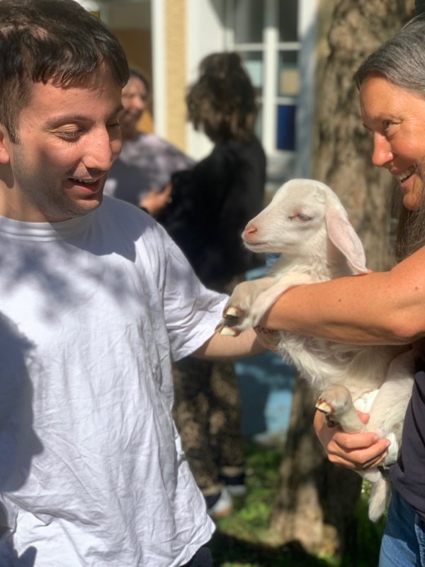 Auf dem Bild sieht man einen Jungen, der ein Lämmchen streichelt, das eine Frau in der Hand hält.