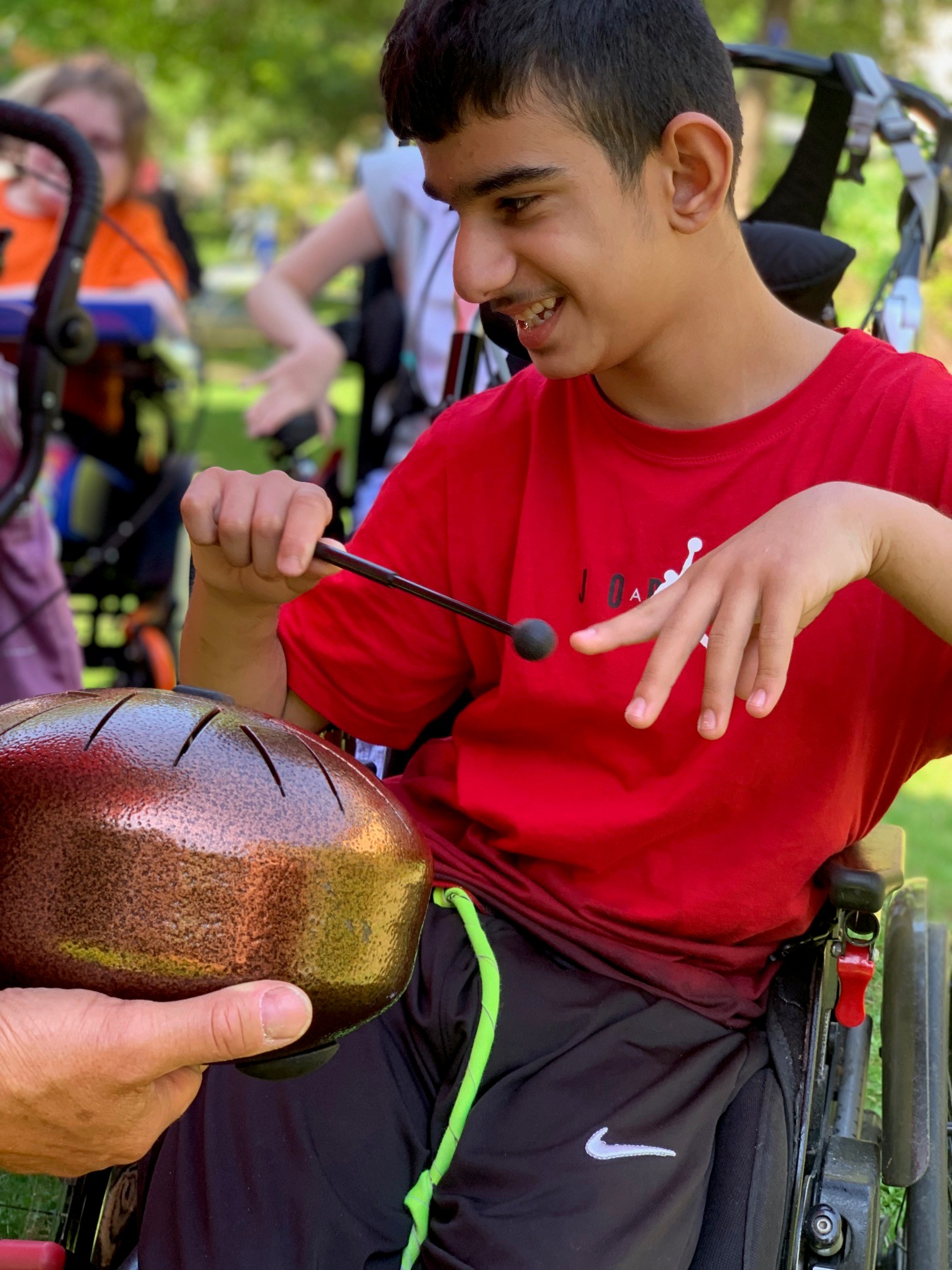 Auf dem Bild sieht man einen Jungen mit rotem T-Shirt, der mit einem Schlegel ein Klanginstrument spielt.