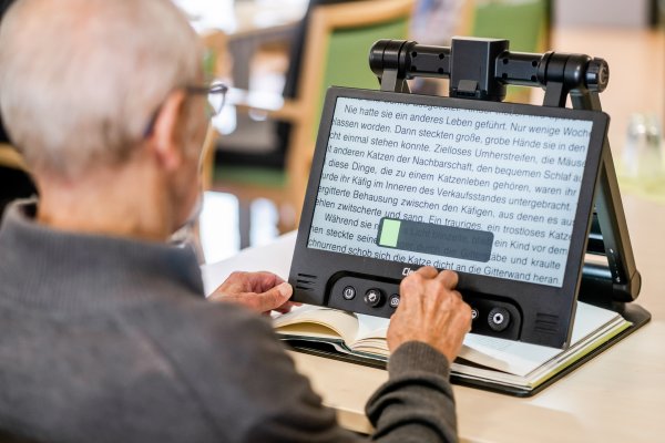 Ein älterer Mann nutzt ein Bildschirmlesegerät zur Vergrößerung eines Buches.