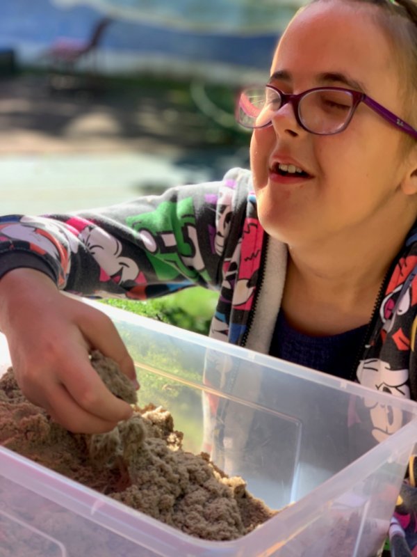 Auf dem Bild sieht man ein Mädchen, das mit seinen Händen Sand in einer Schüssel fühlt