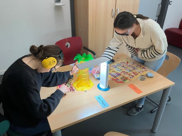 Zwei Frauen mit Simulationsbrillen sitzen an einem Tisch gegenüber und versuchen Aufgaben zu lösen.