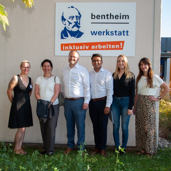Gruppenbild, das sechs Personen vor einem Gebäude mit der Aufschrift bentheim werkstatt - inklusiv arbeiten! zeigt.