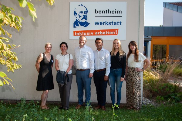 Gruppenbild, das sechs Personen vor einem Gebäude mit der Aufschrift bentheim werkstatt - inklusiv arbeiten! zeigt.