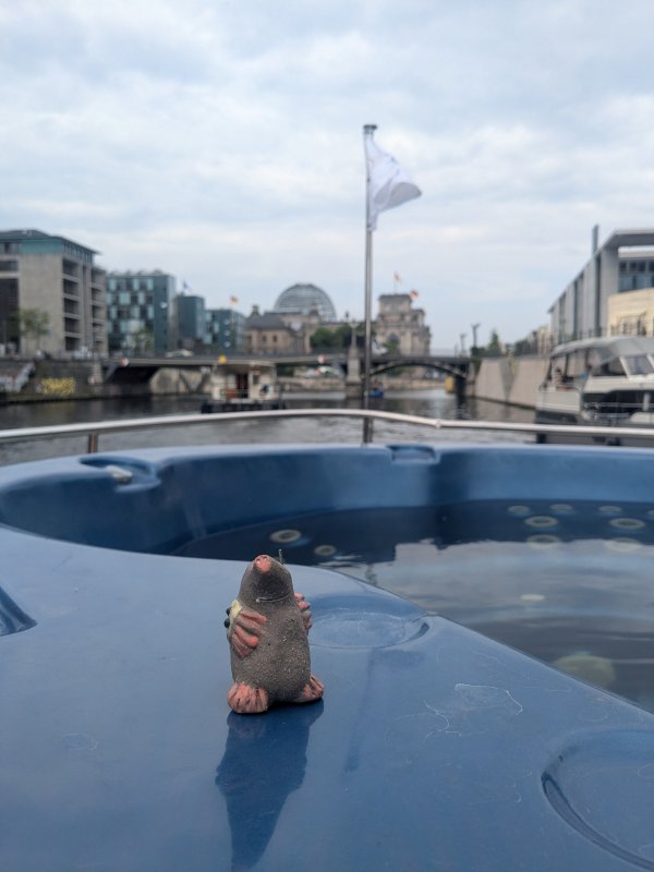Das Bild zeigt einen Maulwurf aus Ton, der auf einem Hausboot durch Berlin fährt.