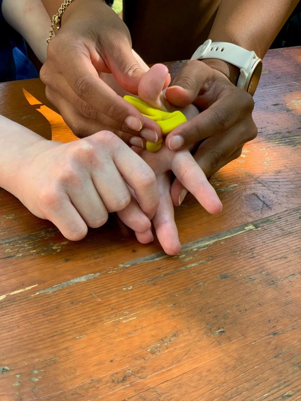 auf dem Bild sieht man wie mehrere Hände einen kleinen gelben Knetball kneten