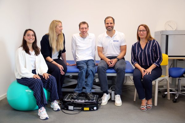 Fünf Menschen sitzen im Halbkreis auf einer Therapieliege und lächeln in die Kamera.