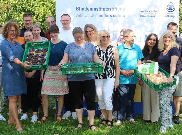 Gruppebild mit fünfzehn Personen in zwei Reihen aufgestellt. In der vorderen Reihe halten drei Personen jeweils einen Korb mit Donuts in der Hand.