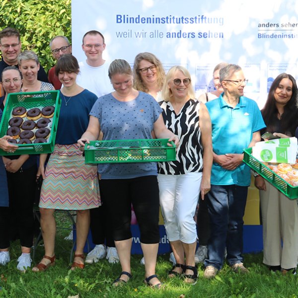 Gruppebild mit fünfzehn Personen in zwei Reihen aufgestellt. In der vorderen Reihe halten drei Personen jeweils einen Korb mit Donuts in der Hand.