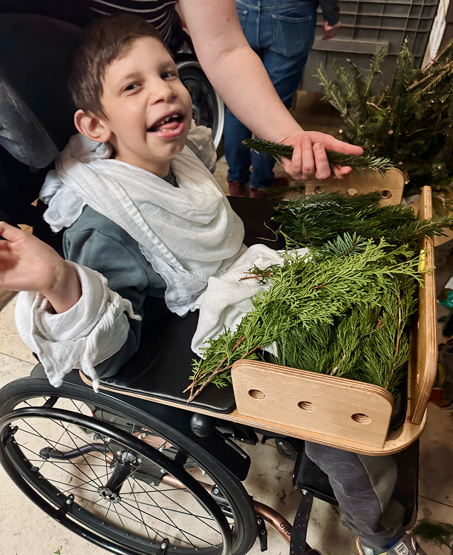 Ein freudiges Kind in einem Rollstuhl erfühlt verschiedene Arten von Tannenzweigen.