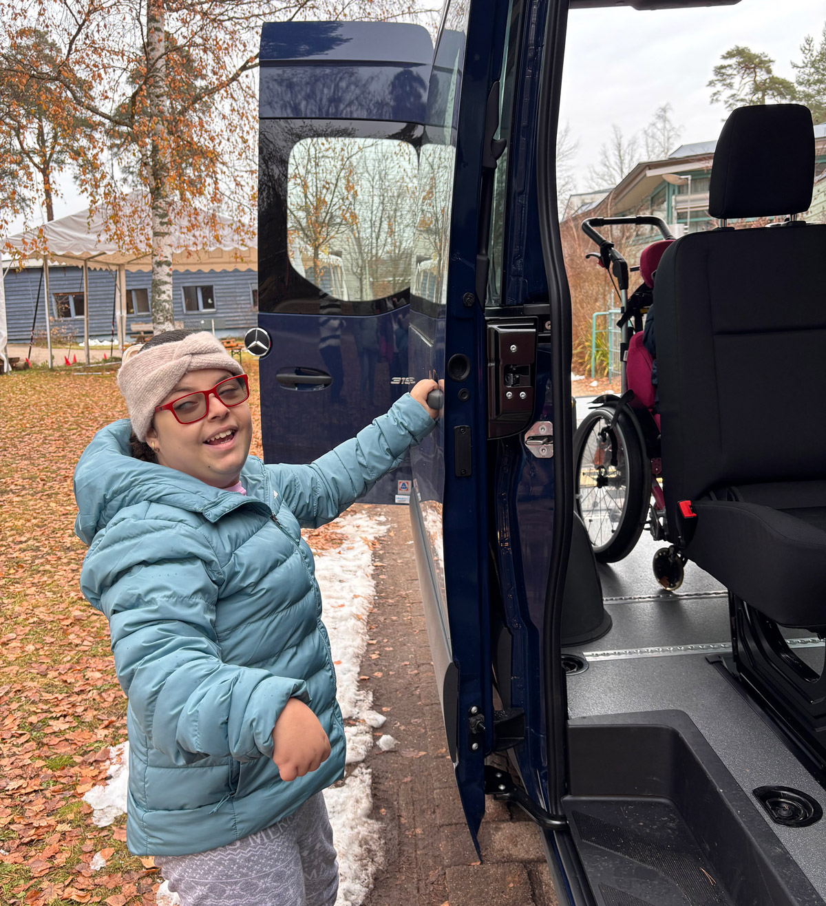Person steht neben der geöffneten Tür eines barrierefreien Busses und bedient die Einstiegsvorrichtung. Im Inneren des Busses ist ein Rollstuhl sichtbar. 