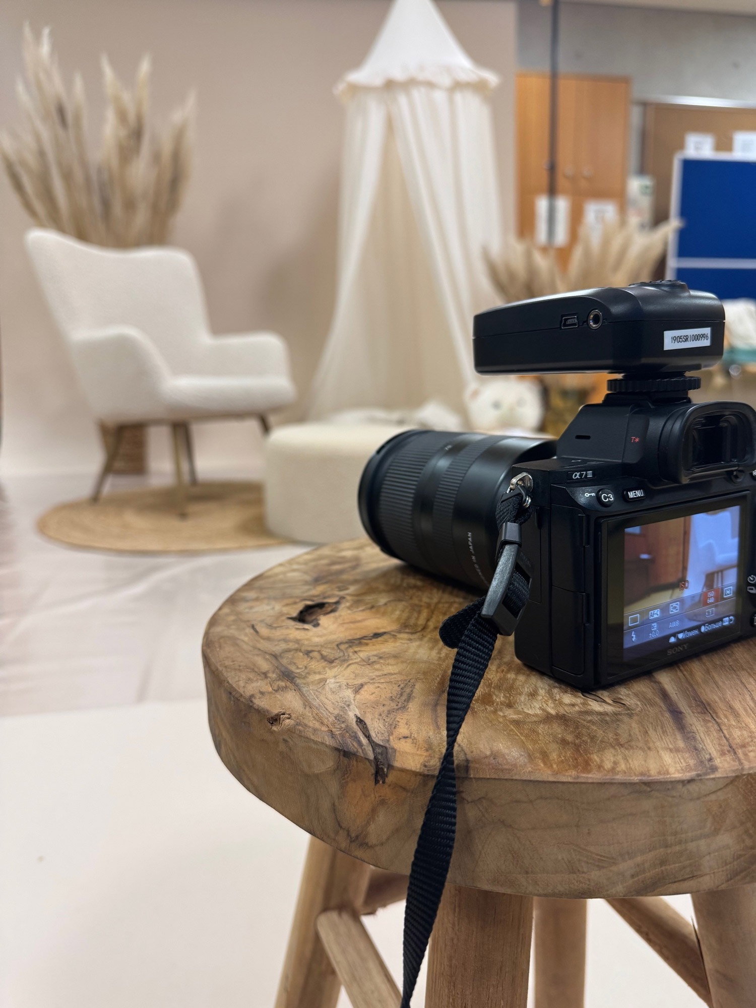 Eine professionelle Spiegelreflexkamera auf einem Holzhocker vor einem neutral gestalteten Fotostudio-Set mit Sessel und Dekoration im Hintergrund, vorbereitet für ein Fotoshooting.