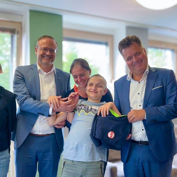 Maria Rascher-Wolfring (Lehrkraft Graf-zu-Bentheim-Schule), Dr. Marco Bambach (Vorstand Blindeninstitutsstiftung), Stefanie Tröster (Gruppenleitung Blindeninstitut Würzburg), Lucas (Schüler Graf-zu-Bentheim-Schule), Jürgen Dusel (Beauftragter der Bundesregierung für die Belange von Menschen mit Behinderungen) und Dr. Michael Weis (Institutsleitung Blindeninstitut Würzburg) sind von links nach rechts auf dem Bild zu sehen. Lucas steht in der Mitte und hält eine kleine, orangene Seepferdchen-Figur in der Hand. Alle lächeln und freuen sich.