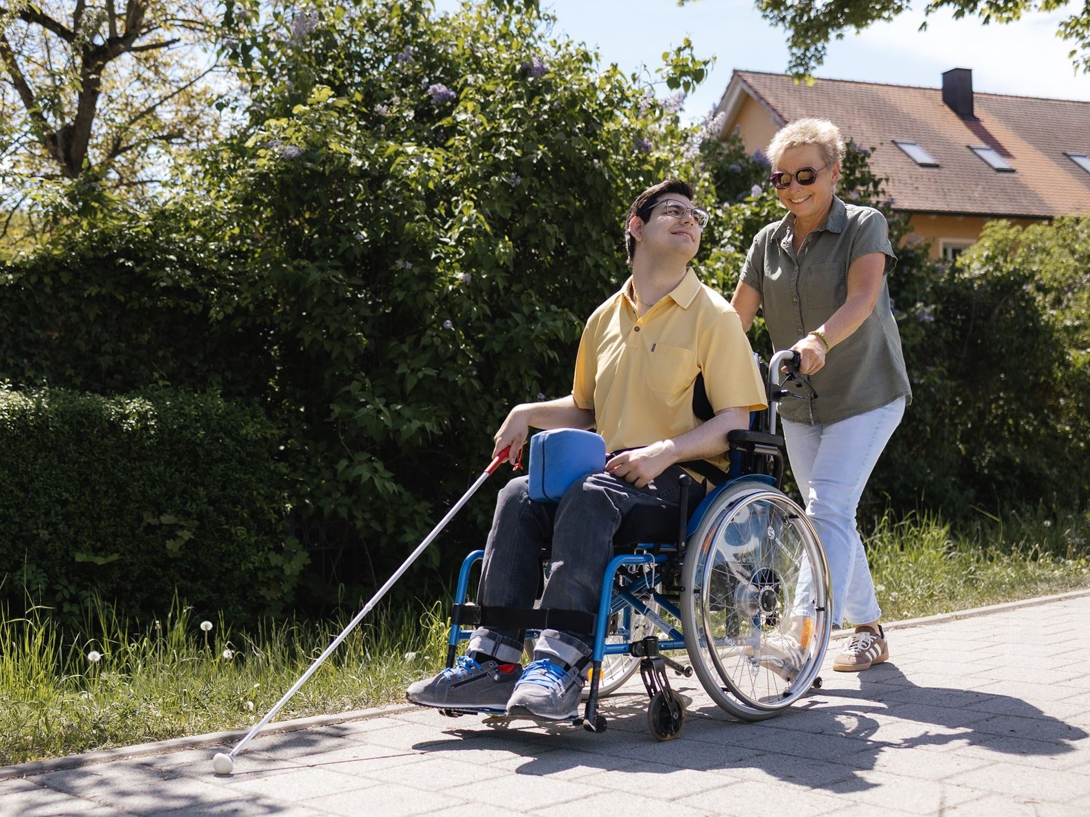 Orientierung und Mobilität: Ein Klient übt mit einer Mitarbeiterin die Orientierung mit dem Langstock. Er sitzt im Rollstuhl.