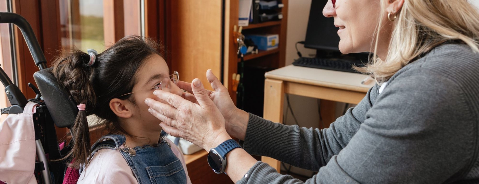 Eine Situation in der Orthoptik. Eine Mitarbeiterin rückt einer Schülerin die Brille zurecht.