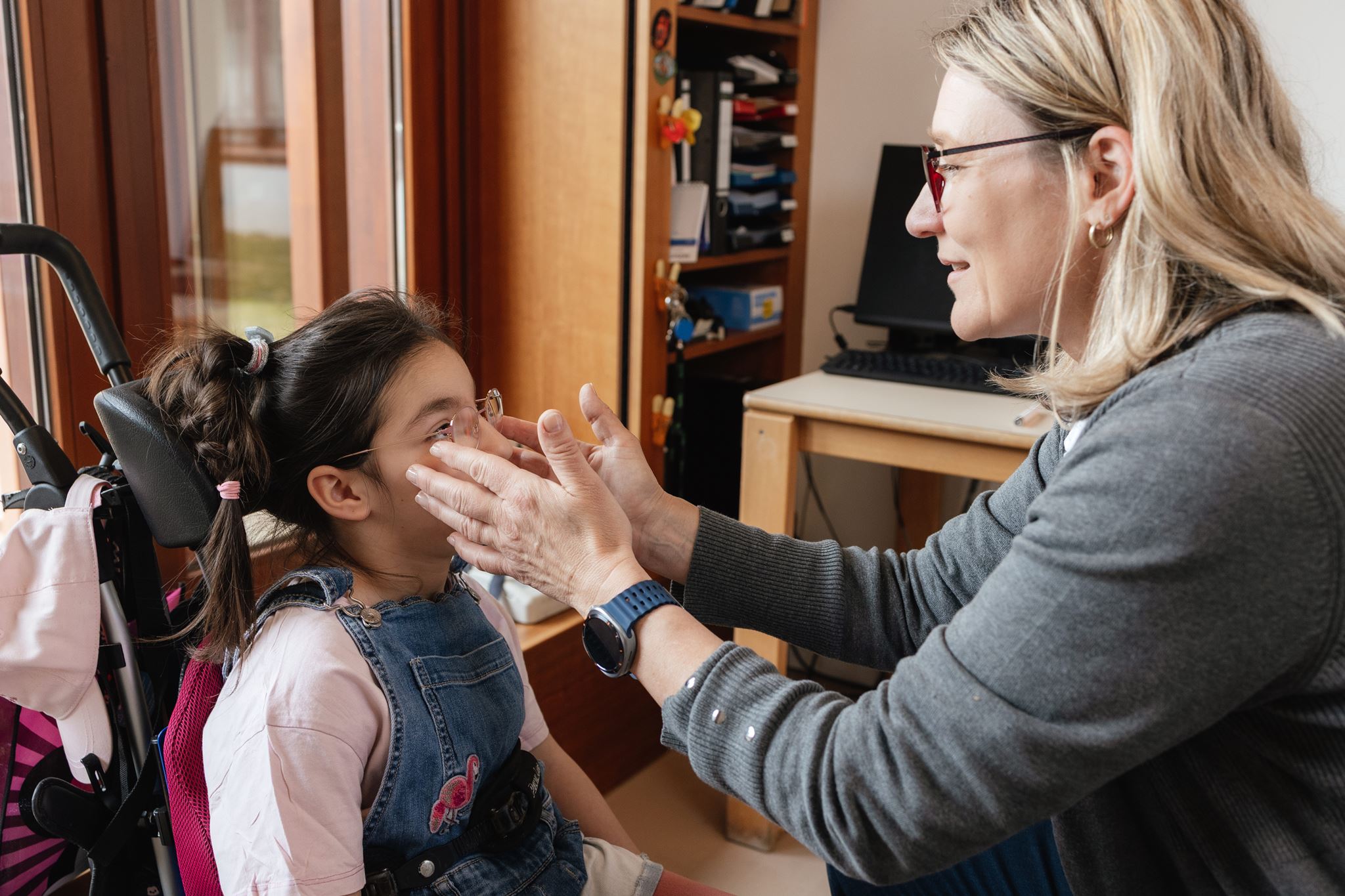 Eine Situation in der Orthoptik: Eine Mitarbeiterin rückt einer Schülerin die Brille zurecht für den anstehenden Sehtest
