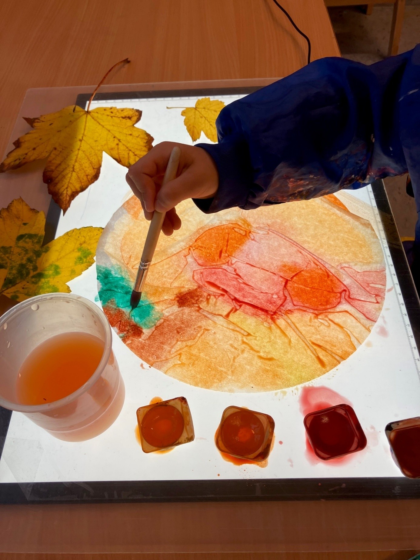 Auf dem Bild sieht man eine Hand, die mit Wasserfarben etwas Buntes malt. 