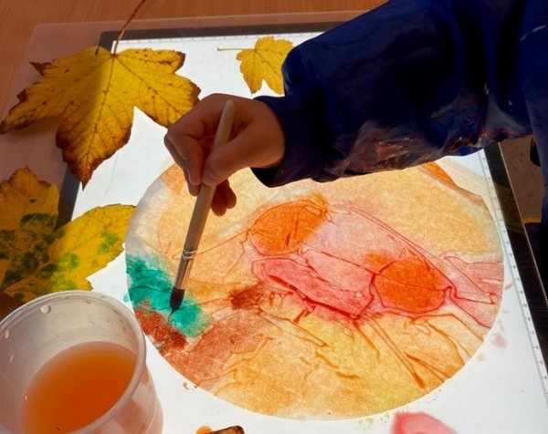 Auf dem Bild sieht man eine Hand, die mit Wasserfarben etwas Buntes malt.