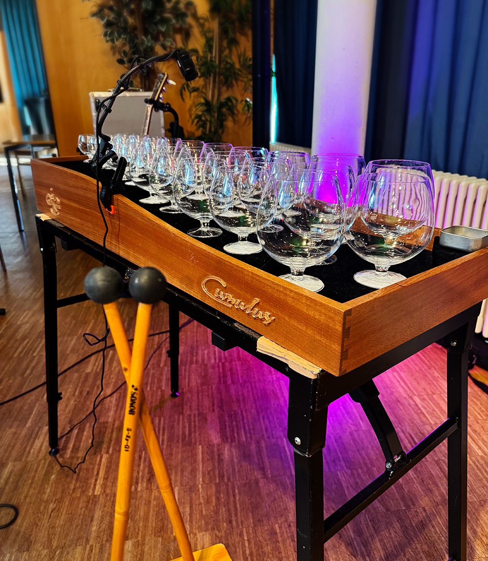 Es ist ein Tisch im Schachbrettmuster zu erkennen, auf dem viele bauchige Gläser stehen, welche als Instrumente dienen.