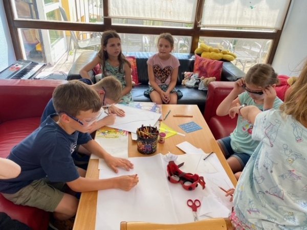 Einige Kinder spielen zusammen an einem vorbereiteten Tisch mit Simulationsbrillen und Malzeug.